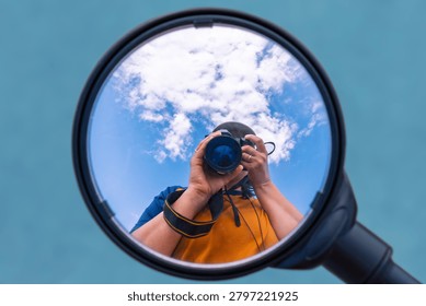 Photographer capturing self reflected in round magnifying mirror outdoors.