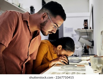 Photographer, editing and film negatives with looking, magnifying glass for zoom analysis at photo journalist job. Photography man, analyse or focus with woman in studio for creative decision in team - Powered by Shutterstock