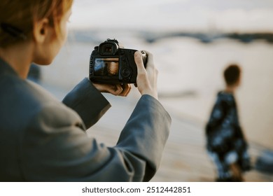 Photographer holding camera capturing scenic sunset over waterfront with blurred person in background providing depth and context. Scene includes serene water and peaceful atmosphere - Powered by Shutterstock