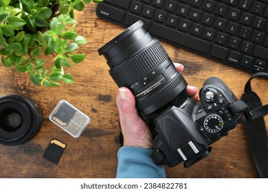 Photographer holding DSLR camera with zoom lens at desk with SD cards and computer keyboard