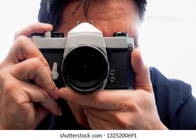 Photographer holding a old film photo camera  on is hand in front of is face - Powered by Shutterstock