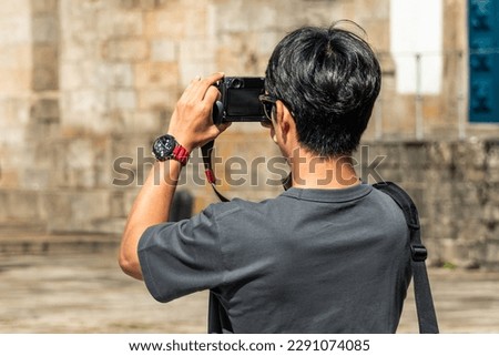 A photographer holds a camera while capturing an impressive architectural scene from behind. An adult enjoys the activity of photographing with modern technology while traveling.