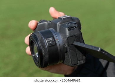 A photographer holds a digital camera, adjusting the lens while surrounded by lush greenery on a sunny day, ready to capture beautiful landscapes - Powered by Shutterstock - Get 15% off with code: PIKWIZARD15