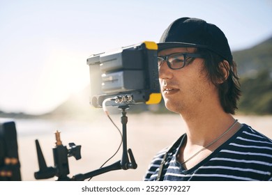 Photographer, man and filming with camera on beach for nature scenery, coastline images or videography. Portable technology, cameraman or person with recording equipment by ocean for content creation - Powered by Shutterstock