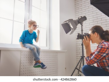 Photographer In Motion. Young Woman Photographer And Child Girl Having Fun At The Photo Session.