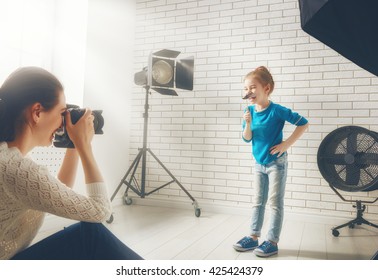 Photographer In Motion. Young Woman Photographer And Child Girl Having Fun At The Photo Session.