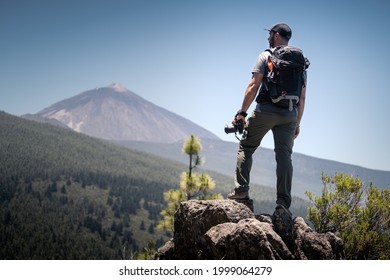 A photographer observes the horizon with his camera in hand from the top of a mountain. You see the landscape with forests, mountains and a volcano. Travel or adventure concept.