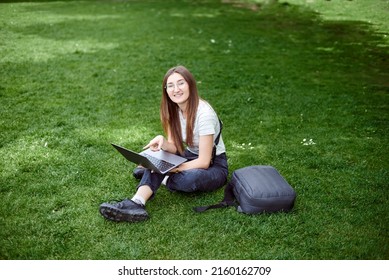 The photographer processes the images on the street. A young girl works with a laptop in the fresh air in the park, sitting on the lawn. Work as a freelancer. The concept of a remote office. - Shutterstock ID 2160162709