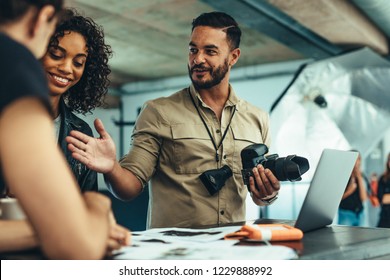 Photographer reviewing the photo shoot with his team on a laptop. Man holding camera discussing photo shoot with his team. - Powered by Shutterstock