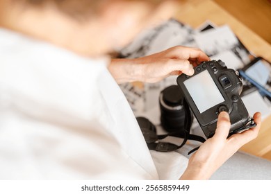 Photographer reviewing photos on a digital camera display in a home office setup, surrounded by photography equipment and prints, showcasing the process of image selection and post-production - Powered by Shutterstock