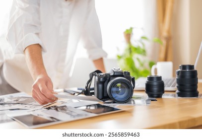 Photographer reviewing printed pictures of stunning landscapes on a desk at home, surrounded by professional camera gear and photography equipment, immersed in creative work - Powered by Shutterstock