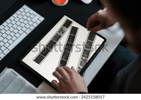 A photographer scrutinizes film negatives on a digital tablet, bridging traditional photography with contemporary technology in his studio