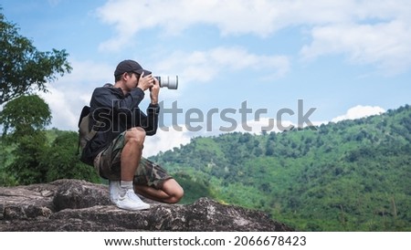 Photographer sits on a cliff with a beautiful mountain landscape in the background. Travel concept adventure active vacations outdoor