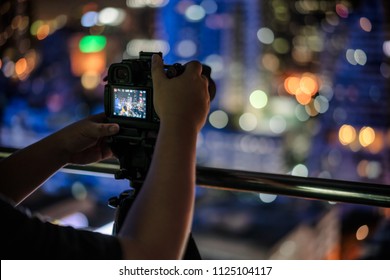 Photographer take a photo with tripod and his camera in the night city.