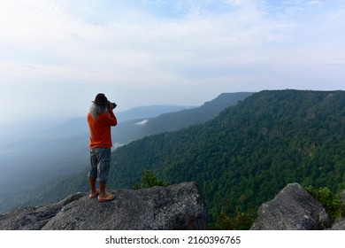 Photographer takes photos of the landscape on  top of the rock mountain at In the morning and light fog in the middle of the perfect natural forest background