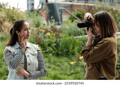 Photographer takes photos of a model posing in a park in an urban setting, surrounded by greenery and with a blurred background - Powered by Shutterstock