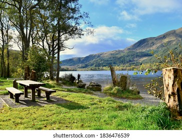 Photographer taking a photo of Loch Lubnaig, surrounded by beautiful trees and  mountains with a picnic bench in foreground. Trossachs, scotland UK. OCTOBER 2020