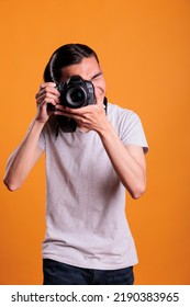 Photographer taking photos on professional digital camera, looking in viewfinder. Young asian man using photographing equipment, front view medium shot, creative hobby, photoshoot