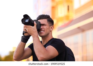 Photographer taking picture with professional camera on city street at sunset