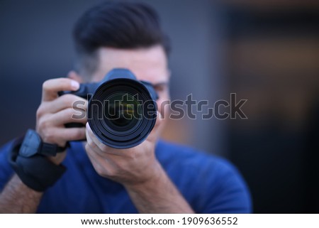 Photographer taking picture with professional camera outdoors in evening, focus on lens