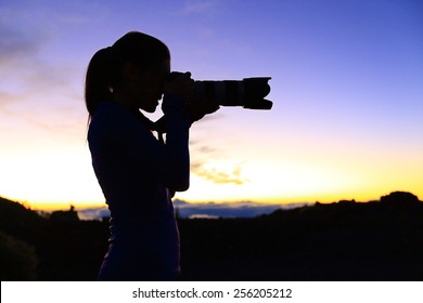 Photographer taking pictures with SLR camera at night. Nature landscape photographer with telephoto lens. Silhouette of woman taking photo after sunset.