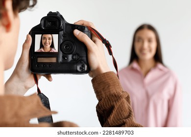 Photographer taking portrait photo of young beautiful woman in photostudio, focus on working digital camera during photoshoot, blurred background - Powered by Shutterstock