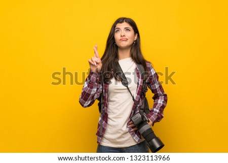 Photographer teenager girl over yellow wall with fingers crossing and wishing the best