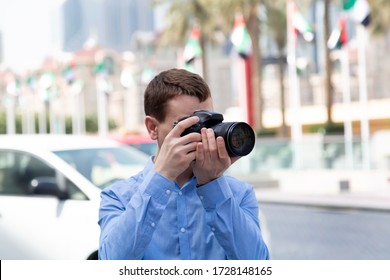 Photographer Tourist On The Streets Of Dubai. A Male Photographer Paparazi In A Blue Shirt Is Watching An Object Taking Photos