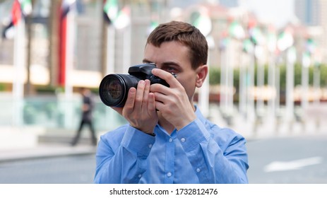 Photographer Tourist On The Streets Of Dubai. A Male Photographer Paparazi In Blue Shirt Is Watching An Object, Taking Photos.