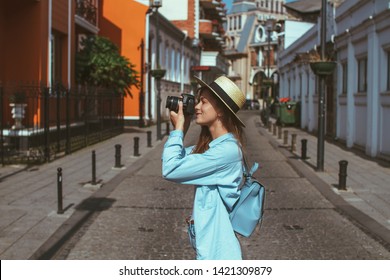 Photographer Traveler In Hat And With Backpack Takes Pictures Of Sights While Walking Along The Street Of A European City. Vacation And Travel Holidays. Traveling Lifestyle