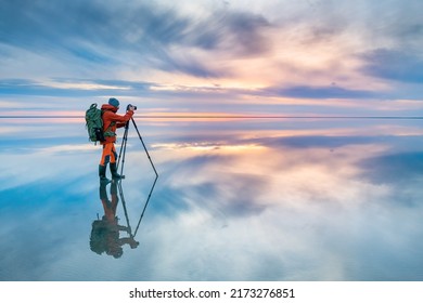 Photographer traveler taking photo of the salt lake at sunset. Blue sky with clouds are reflected in the mirror water surface. Professional photographer using tripod and dslr camera 