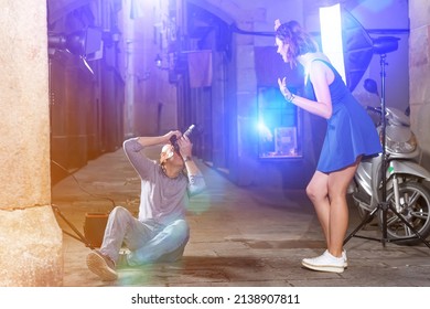 Photographer Using Professional Camera And Light Equipment For Taking Pictures Of Laughing Woman In Blue Dress On Town Street