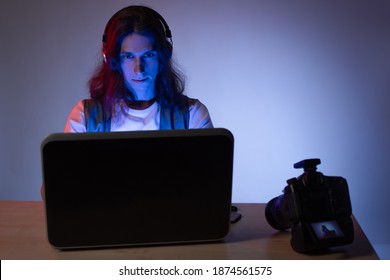 photographer or videographer processes media content on a laptop, a blogger guy works at a computer, a portrait in dark colors, neon tinting