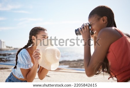 Photographer, woman and model at the beach in summer shooting a creative, freedom and happy outdoor pictures. Photography, smile and fun girl holding a camera with focus on female and ocean backdrop