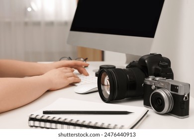 Photographer working on computer at white table with cameras indoors, closeup - Powered by Shutterstock