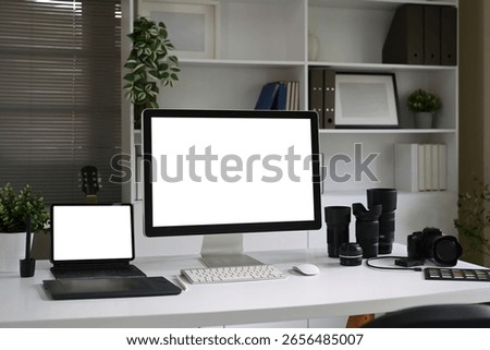 Photographer workspace with computer, tablet, camera and lenses on a white desk in creative studio