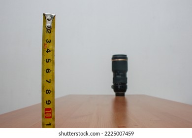Photographers' equipment. A lens in the distance with a meter in close-up on a brown table and a white background.