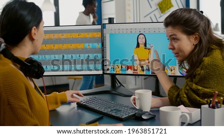 Photographers using professional retouching software or application to edit photos with stylus pen, discussing in front of computer with dual monitors setup. Project managet pointing on display.