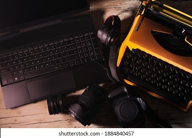 Photographic and office equipment for photojournalists with vintage typewriter, laptop, camera and photographic lenses on a desk in an overhead shot from top to bottom