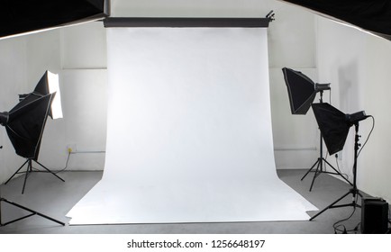 A Photographic Studio With Studio Flashes And A White Seamless Backdrop, From The Vantage Point Of The Photographer.