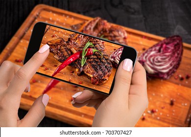 Photographing Food Concept - Tourist Takes Picture Of Ready-to-eat Beef Steak Dish On Cutting Wooden Board On Smartphone.