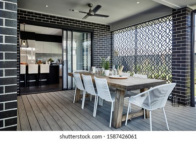 Photography Of Al Fresco Setting At Rear Of Modern Dark Brick Family Home With Outdoor Table Furniture Setting On Decking Area With View To Inside Of Kitchen Area With Breakfast Bar