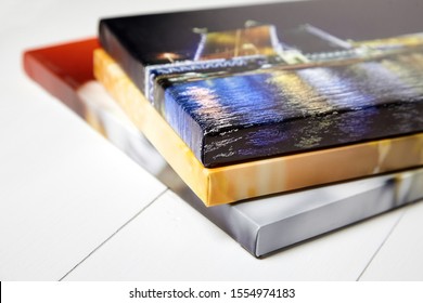 Photography canvas prints. Stack of colorful photos with gallery wrap on white wooden table. Stretched photo canvases, lateral side, closeup