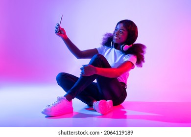 Photography Concept. Smiling Young Black Woman Taking Selfie In Neon Light, Full Length. Happy African American Lady Looking At Camera, Making Self Portrait For Social Media Or Her Blog