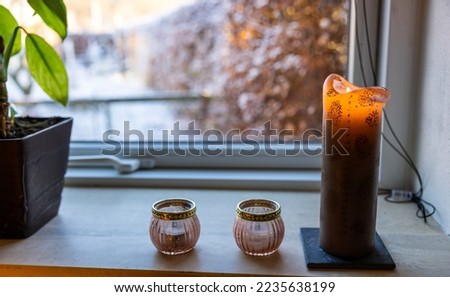 A photography of a Danish advent calendar candle known as kalenderlys lighting near a window with view of garden in winterseason.