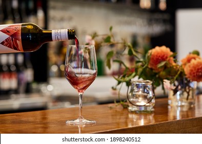 Photography of a glass of red wine being poured into a wine glass on a counter top in a bar