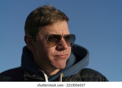 Photography Of Handsome Man. Spring Warm Sunny Day. Blue Clear Sky As Background. Close Up Beautiful Image. Portrait. He Smiles Skeptically. He Pouted.