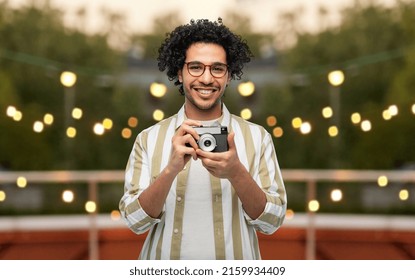 Photography, Profession And People And Concept - Happy Smiling Man Or Photographer In Glasses With Film Camera Over Party Lights On Roof Top Background