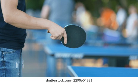 Fotografía de una pequeña raqueta en la mano de un jugador en la calle de la ciudad en el día de primavera. Es un murciélago de madera laminada cubierto de caucho en dos lados. El juego es rápido, exige reacciones rápidas