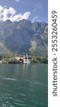 photography of the St. Bartholomew Church on lake Königsee in Germany. the church is on the lake shore, with mountains in the background

